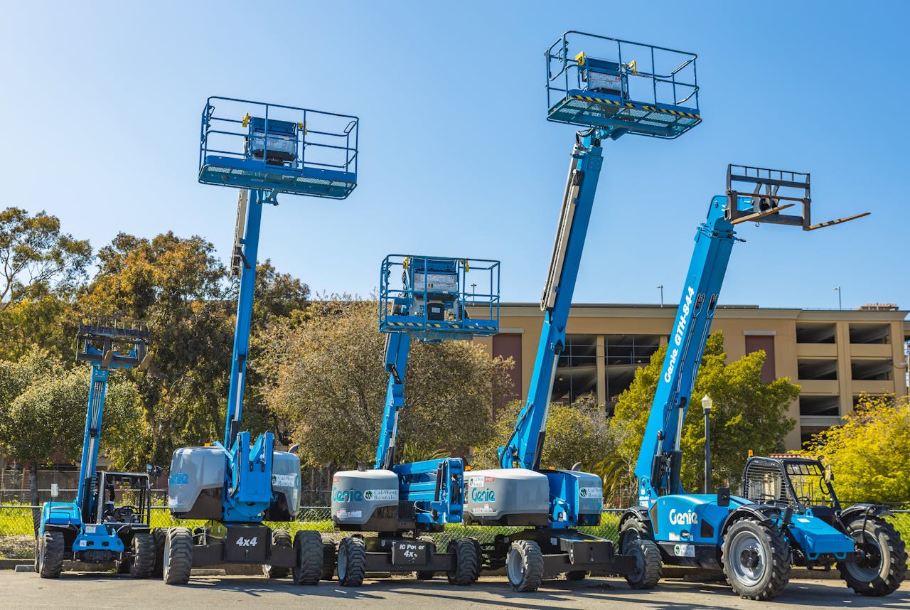 Outdoor scene with multiple blue aerial lifts and heavy machinery in a sunny industrial area.