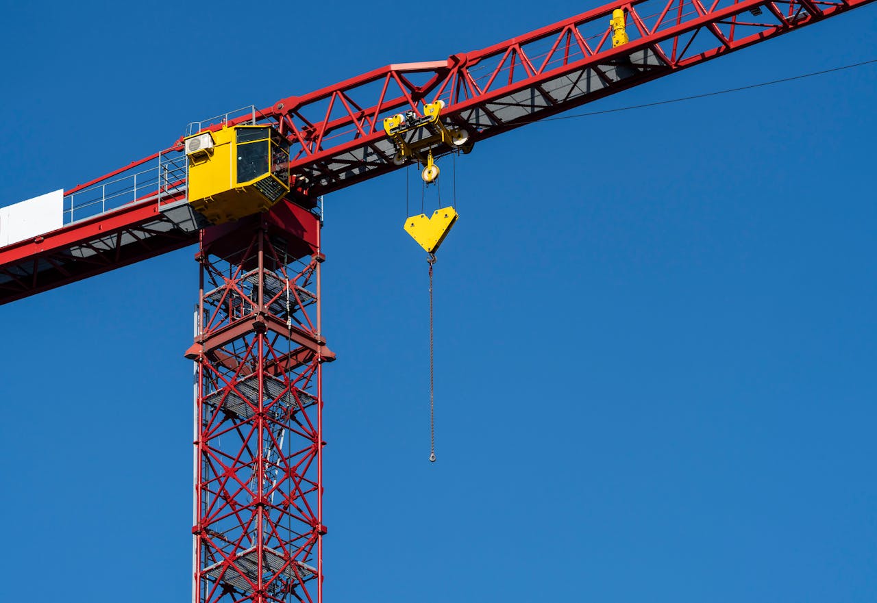 A vibrant red and yellow tower crane set against a clear blue sky, emphasizing construction site themes.
